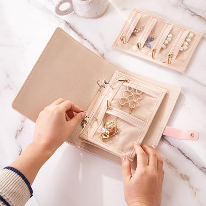 Person organizing jewelry in a beige jewelry organizer on a marble surface.